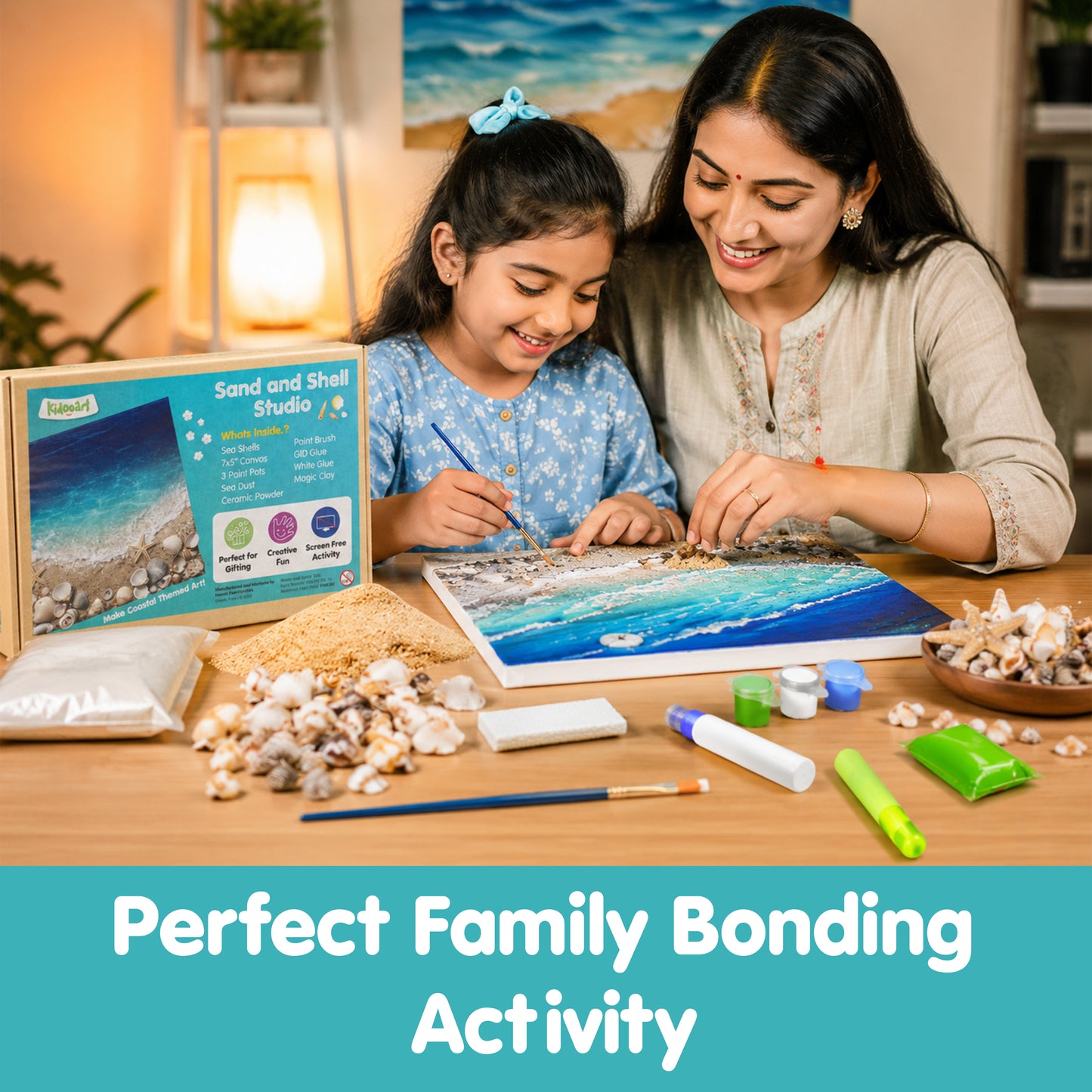 A woman and a young girl are sitting together at a wooden table, working on a sand and shell studio craft kit that forms a blue ocean wave design. The kit includes various shells, sand, paint tubes, and a box labeled 'Sand and Shell Studio'.